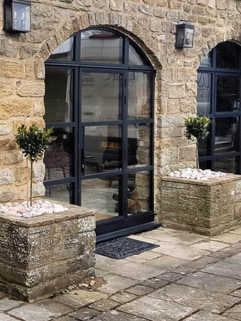 Bespoke heritage aluminium arched window and door system installed on a stone property with modern glazing.