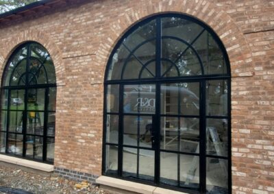 Arched heritage aluminium windows with slim black frames installed on a brick building.