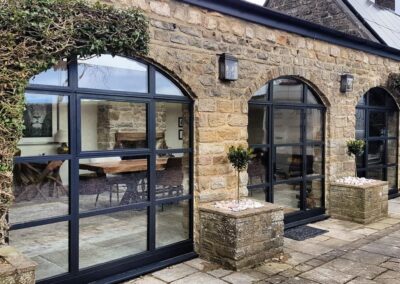 Arched heritage aluminium windows with slim black frames installed on a traditional stone property.