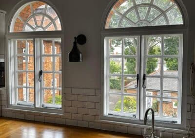 Arched heritage aluminium windows with white frames above a kitchen sink and wooden countertop.