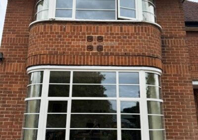 Curved heritage aluminium bay windows with white frames on a brick building.