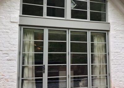 Large heritage aluminium gable window with slim black frames on a white brick house.