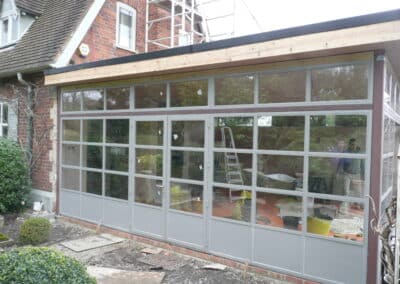 Heritage aluminium glass extension with grey frames attached to a brick house during construction.