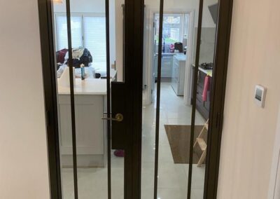 Heritage aluminium internal glass doors with dark frames opening into a modern white kitchen.