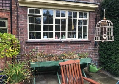 Heritage aluminium multi‑pane window with a cream frame on a brick house overlooking a garden patio.