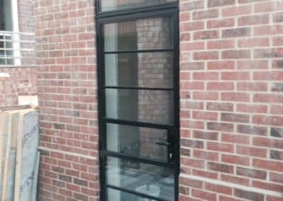 Tall heritage aluminium slimline glass door with a black frame set into a red brick wall.