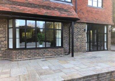Heritage aluminium windows with slim black frames installed on a brick property overlooking a stone patio.