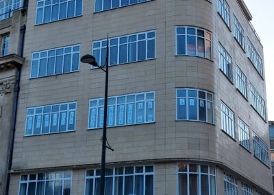 Heritage aluminium windows with slim black frames on a beige‑tiled commercial building above shopfronts.