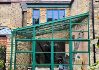 Green aluminium framed glass extension attached to a traditional brick house.