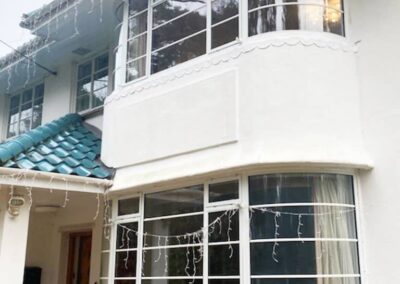 Two‑storey house with white curved bay windows, teal roof tiles and decorative exterior lighting.